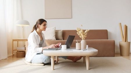 Woman working on a laptop in a bright, minimalist home office with neutral décor—illustrating a comfortable remote-work setup for using Typinator productivity tools in Europe.